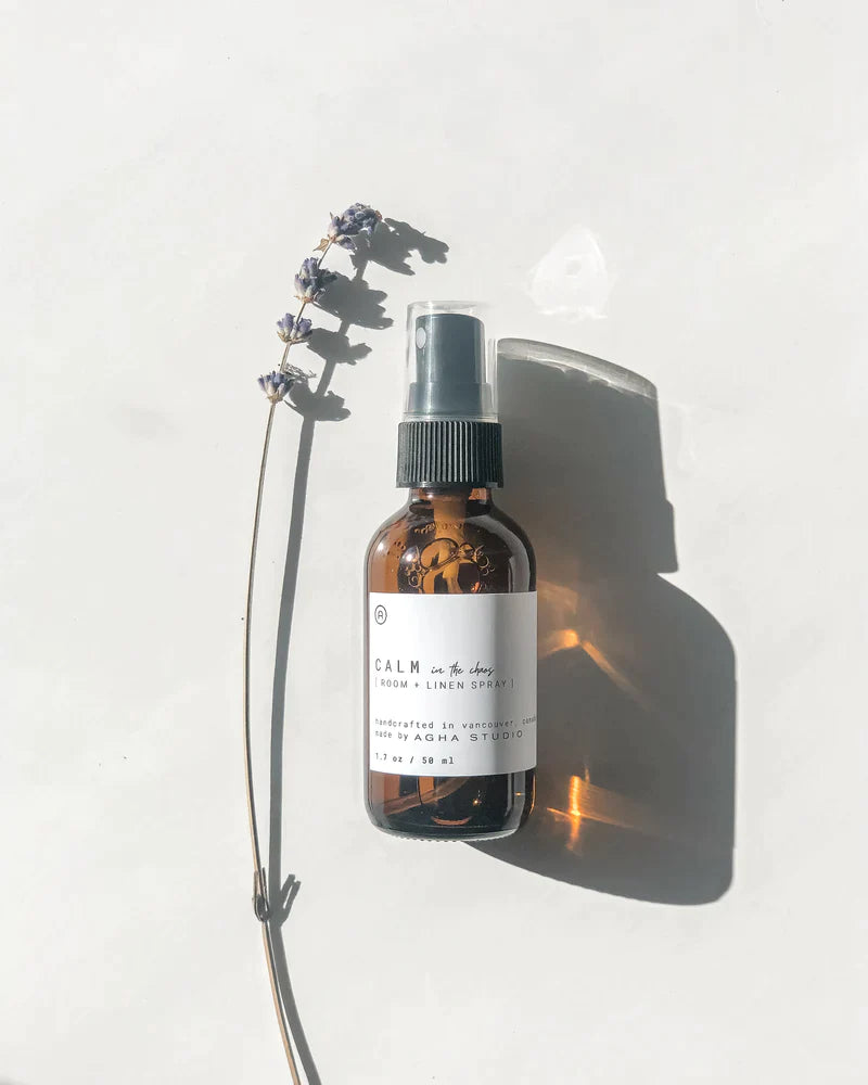 Room and linen spray made with all natural ingredients and essential oils by Agha Studio, with a lavender branch representing the ingredients.