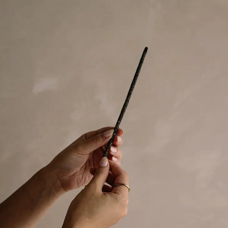 A burning incense stick held by a person's hands.