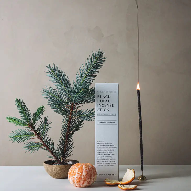 An incense stick in an incense holder that is lit and burning, along with its box by Cedar and Myrrh.