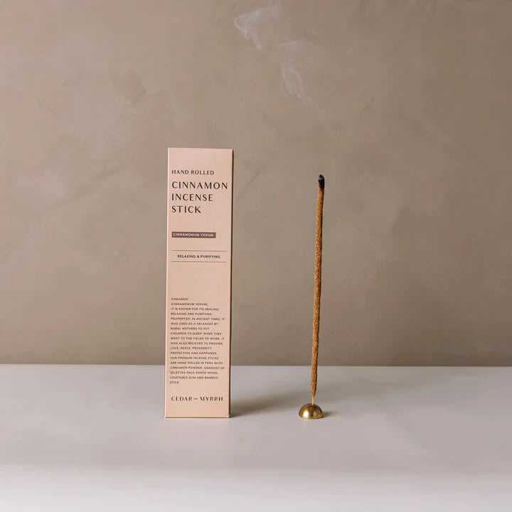 A burning hand-rolled incense stick by Cedar and Myrrh in an incense holder and its box.