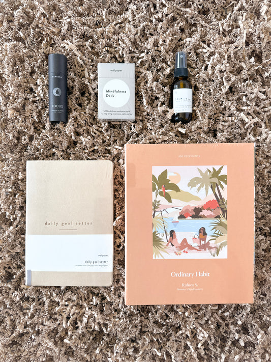 Care packages curated with products to promote mindful living and mental wellness including a jigsaw puzzle by Ordinary Habit, a journal by Mal Paper, an essential oil blend from Bursera, an aromatherapy mist by Agha Studio and a mindfulness card deck.