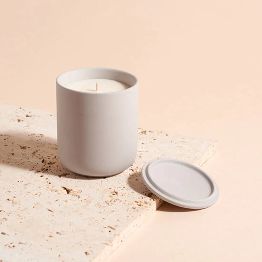 Candle in a light grey ceramic vessle by Lit By drew, with the lid on the side, in cotton and musk scent adding fragrance to a home.