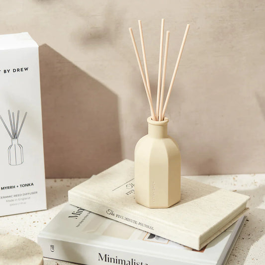 A reef diffuser in a beige container with wooden reeds by Lit By Drew, on a desk adding elegance to the decor and aroma to the space in myrrh and tonka scent.