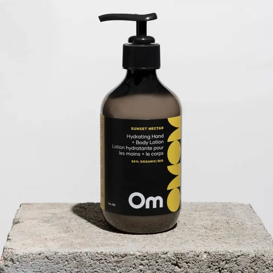 The bottle of a hand and body lotion in lime and clary safe scent by Om Organics, sitting on a surface with the sun shining and the shadow of the bottle on the surface.