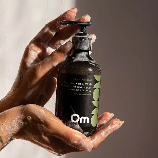 A woman holding a bottle of hand and body wash by Om Organics in Lime and Clary Sage scent, with the foam from the hand and body wash covering her hands.