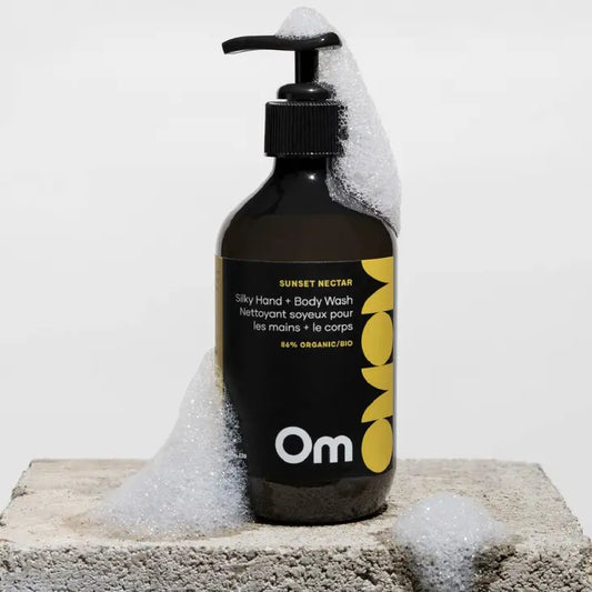 A bottle of natural hand and body lotion from Om Organics in Sunset Nectar scent which has mango and vanilla bean extract, sitting on a surface with the foam from the hand and body wash covering the bottle.