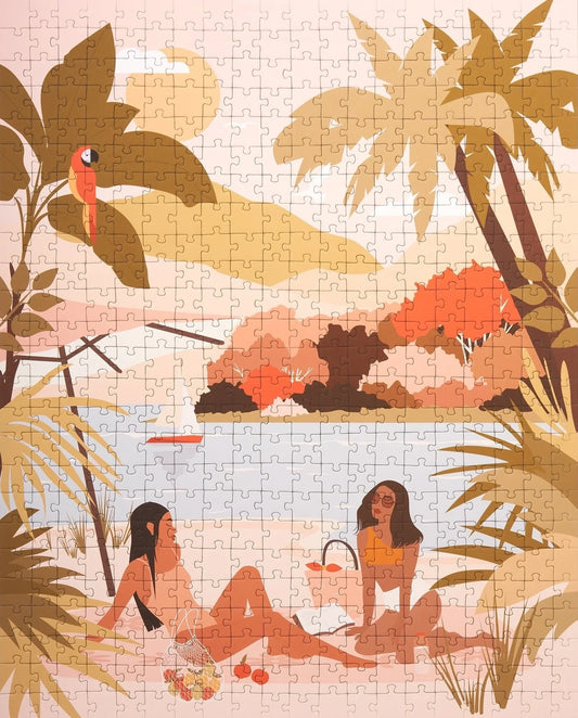 A completed 500 piece puzzle by Ordinary Habits showing two girls sitting on the beach having a picnic by the water and amongst palm trees.