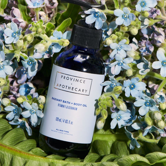 Bottle of bath and body oil by Province Apothecary amongst flowers and leaves showcasing its natural ingredients.