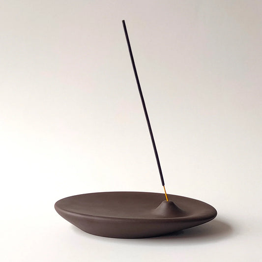 An incense holder in dark brown color, handmade with ceramic stoneware by Siesta Studio, Turkey, holding an incense stick.